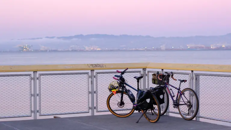A blue Kona e-bike and purple vintage Trek in front of a view of the San Francisco Bay facing towards the East Bay, some time after the sun has set
